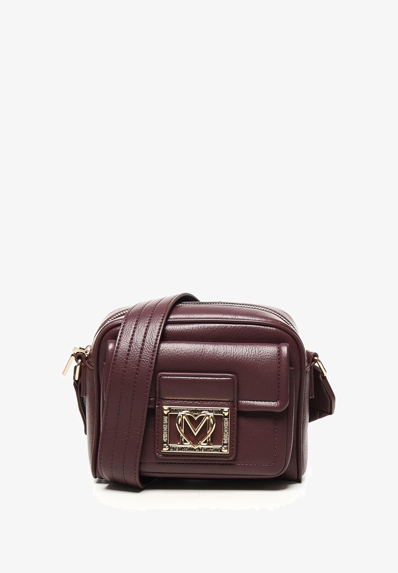 Piccola borsa a tracolla in pelle marrone scuro con tracolla larga e placca logata in metallo dorato sulla tasca anteriore.