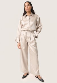 Satin beige långärmad skjorta med knappar och vida byxor. Svarta slipskor med en texturerad yta. Slät, glansig tyg.