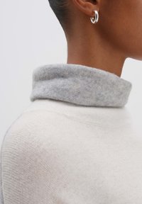 Weißer Strickpullover mit einem weichen grauen gefalteten Rollkragen, der eine strukturierte Webart und ein glattes akzentuiertes Ohrcuff aufweist.