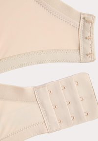 Beige beha-bandjes met haak-en-oogsluitingen, die drie rijen haken en drie kolommen ogen tonen op een stoffen achtergrond.