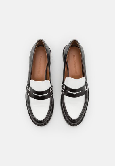 Schwarz-weiße Loafers mit glänzender Oberfläche, ausgestattet mit einer weißen Vorderseite und silberfarbenen Akzenten. Abgerundete Zehen und strukturierte Sohlen.