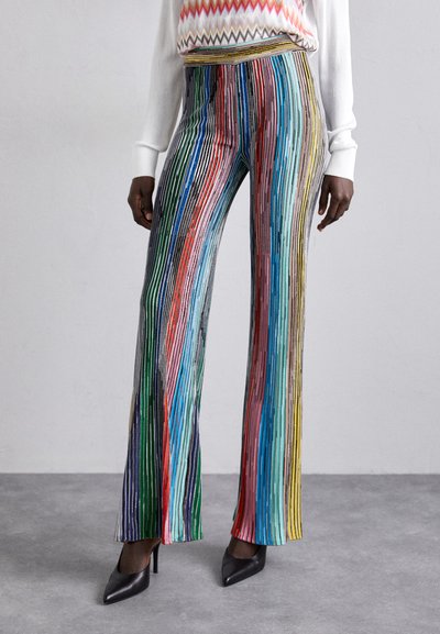 Pantalons rayés verticalement multicolores en tissu léger. Il présente une taille haute et des jambes évasées, associés à des talons aiguilles noirs.
