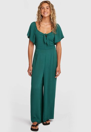 Combinaison sarcelle avec manches courtes volantées, devant noué et coupe évasée. Fabriquée en tissu léger à texture lisse.