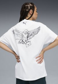 White oversized t-shirt with a black line-drawing of an owl carrying an envelope on the back. Puma logo on the left shoulder. Cotton material.