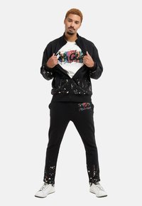 Black track jacket and sweatpants with colorful paint splatter, featuring a white t-shirt with a multicolored graphic design, and white sneakers.