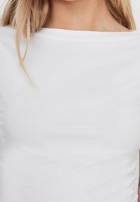 Bílý bavlněný top s lodičkovým výstřihem, hladkým povrchem a krátkými rukávy. Jednoduchý design bez viditelných vzorů nebo ozdob.