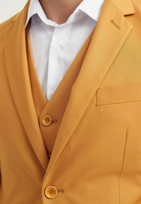 Blazer jaune avec une texture lisse, deux boutons et une poche poitrine. Porté par-dessus une chemise blanche, montrant une coupe moderne et ajustée.