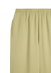Jasnozielone spodnie na gumce wykonane z miękkiego, gładkiego materiału, luźne w kroju. Bezszwowy design bez widocznych zapięć czy kieszeni.