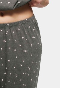 Graue Schlafanzughose mit einem verstreuten pinken Herzmuster, aus weichem Stoff, mit elastischem Bund und entspannter Passform, die für Komfort sorgt.