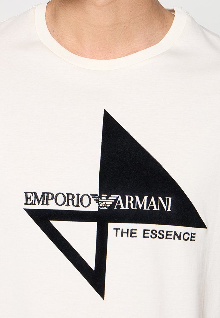 Camiseta blanca con diseño geom étrico negro y texto "EMPORIO ARMANI" y "THE ESSENCE" en el pecho.