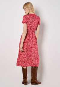 Robe florale rouge avec des manches bouffantes courtes, dos froncé, et longueur mi-mollet. Assortie avec des bottes de cowboy marron.