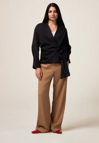 Zwarte blouse met een strikdetail, gecombineerd met beige wijde broekspijpen en rode platte schoenen. Glad materiaal met een stijlvolle uitstraling.