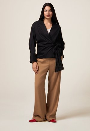 Zwarte blouse met een strikdetail, gecombineerd met beige wijde broekspijpen en rode platte schoenen. Glad materiaal met een stijlvolle uitstraling.