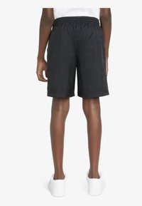 Pantalones cortos deportivos negros con una cinturilla elástica y un ajuste holgado, que llegan a la mitad del muslo, combinados con zapatillas blancas. Textura suave.