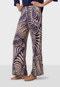 Pantalons à jambe large avec une base crème et des motifs de feuilles bleu marine. Fabriqués en tissu léger, ils offrent une coupe décontractée et une texture douce.