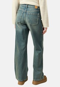 Jeans de mezclilla de pierna ancha en azul claro con un lavado medio, detalles de costura visibles y dos bolsillos traseros, que presentan una etiqueta de marca de cuero.