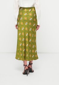 Saia verde estampada com designs de olhos e flores, feita em tecido suave. Cintura ajustada com a parte inferior rodada e saltos altos visíveis.