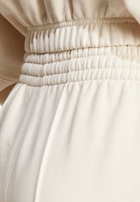 Tasca elastica di un indumento in tessuto color crema, caratterizzata da dettagli arricciati e texture liscia per una vestibilità rilassata.