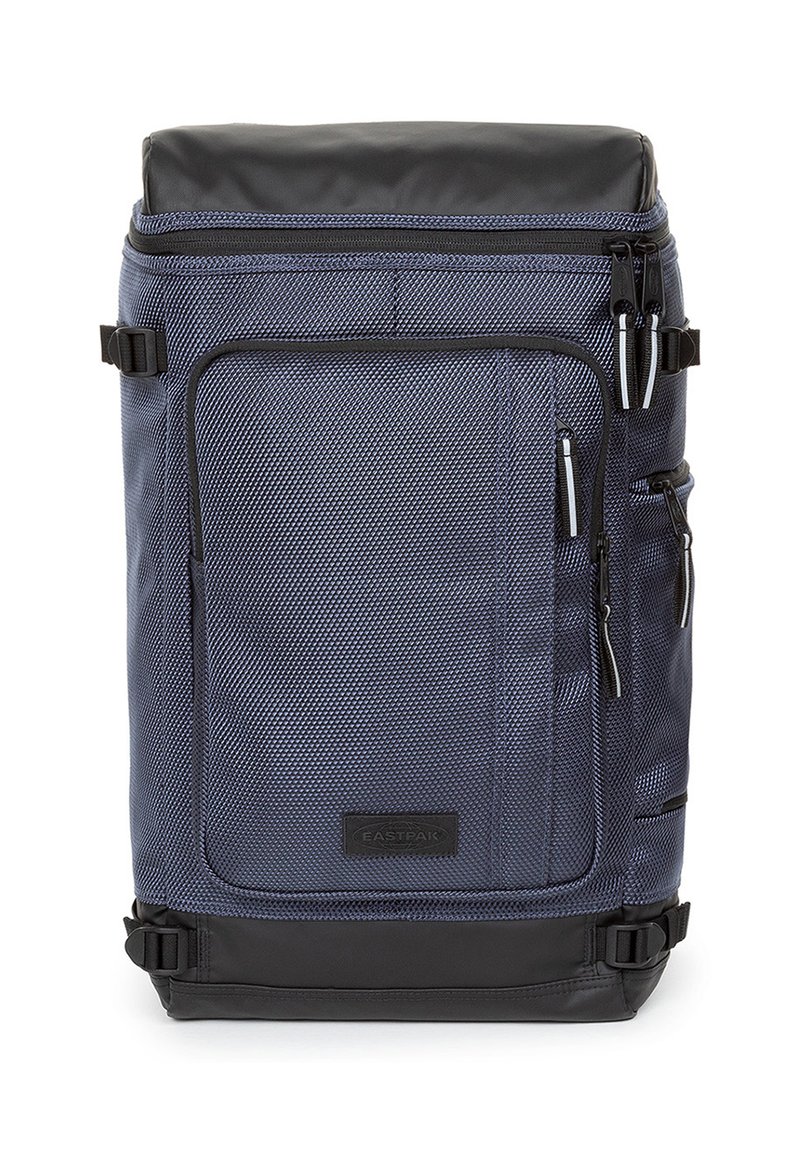 Sac à dos bleu marine avec accents noirs, tissu texturé, plusieurs compartiments zippés, bretelles latérales et un panneau inférieur renforcé.