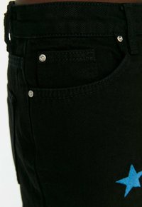 Vaqueros de mezclilla negros con un botón plateado y un diseño de estrella azul en el bolsillo delantero. Tela texturizada con un corte clásico.