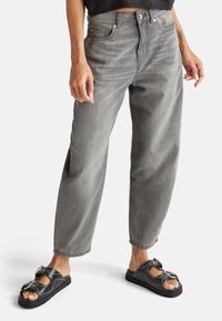 Graue Jeans aus Denim mit lässiger Passform, featuring eine hohe Taille, fünf Taschen und Kupferriegel. Kombiniert mit schwarzen Rutsch-Sandalen mit Hardware-Details.