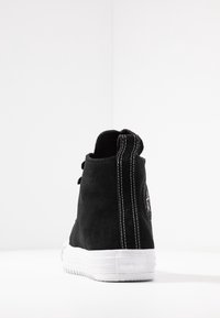 Schwarze Wildleder-Hochtop-Sneaker mit weißer Gummisohle, ausgestattet mit kontrastierenden weißen Nähten, rundem Logo-Patch und Schnürverschluss.