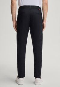 Czarne spodnie wykonane z gładkiego materiału, dopasowany krój, z dwiema tylnymi kieszeniami i subtelnym logo marki. Noszone z białymi sneakersami.