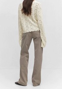 Pull en tricot crème avec un motif ajouré, associé à un pantalon taille haute rayé marron clair. Les deux vêtements ont des coupes décontractées.