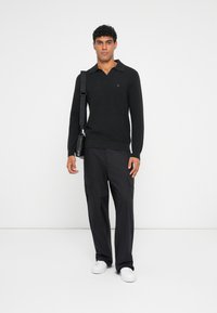 Sort strikket sweater med krave, båret sammen med sorte cargo-bukser og hvide sneakers. Et lille logo er synligt på sweateren.