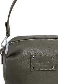 Borsa in pelle verde con superficie testurizzata, chiusura a zip e tracolla removibile. Presenta una placca con logo e dettagli metallici.