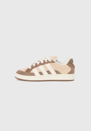 Lavtopsneaker i beige og brun med hvide striber, hvide snørebånd og en gummisål vist fra siden på en ensfarvet baggrund.