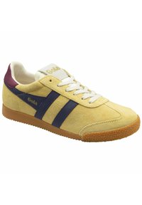 Zapatillas de ante amarillo claro con rayas navy, cordones blancos y un talón burdeos. Presenta una suela de goma texturizada y una lengüeta con marca.