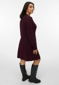 Bordeaux stickad klänning med lång ärm och utställd nederdel. Ett par svarta knähöga stövlar kompletterar outfiten. Enkel och strukturerad design.
