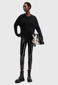 Czarny oversize sweter dzianinowy o luźnym kroju, zestawiony z błyszczącymi czarnymi leggingsami i czarnymi botkami za kostkę na sznurówki. Akcent w postaci srebrnej metalicznej torebki.