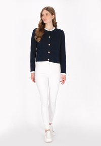 Navy blue button-up jacket with two front pockets, white trim, and textured fabric; worn with white skinny jeans and white sneakers.