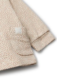 Krémový látkový top s malými terakotovými tečkami, s prošitým okrajem a našitým kapsička s texturovaným logem na rukávu.