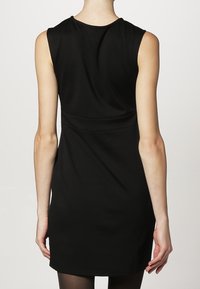 Robe noire sans manches avec une silhouette ajustée, en tissu doux, décolleté rond et détails subtils sur la couture du dos. Design minimaliste.