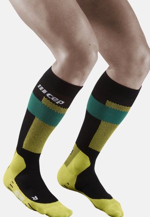 Knielange compressiesokken in zwart, groen en geel. Heeft gestructureerde patronen en een verstevigde teen, met een logo op de bovenband.