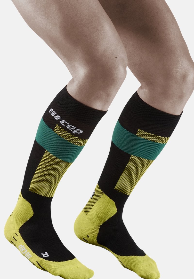 Calze compressive al ginocchio in nero, verde e giallo. Presentano motivi testurizzati e punta rinforzata, con logo sulla banda superiore.