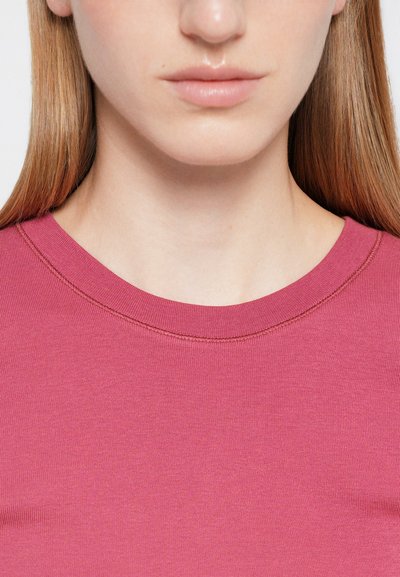 Kerek nyakú, testhez simuló felső egyszínű rózsaszínben, sima, könnyű anyagból készült, finom bordázott textúrával és kontrasztos varrási részlettel.