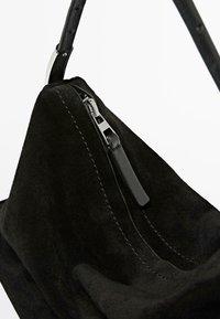 Black suede handbag with zipper closure; features smooth texture, contrasting stitching, and a slender leather strap.