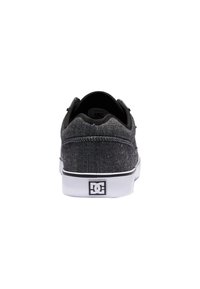 Zapatillas de tela negras con un acabado texturizado, suela blanca y acento de logo en el talón. Diseño sin cordones con una silueta de perfil bajo.