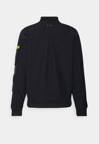 Svart jacka med hög krage, med veckdetalj på baksidan, fickor på ärmarna och en texturerad tyg.