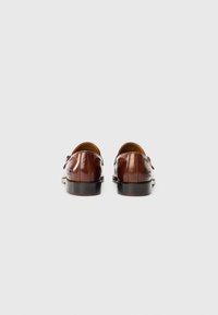 Brown leather shoes with a smooth texture, rounded toe, and low heel. Subtle stitching details and branding on the side.