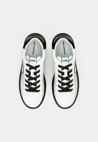 Białe skórzane sneakersy z czarną gumową podeszwą, czarnymi sznurówkami i akcentami logotypu. Gładka tekstura z zaokrąglonym noskiem.