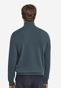 Ciemnoturkusowy sweter z wysokim kołnierzem, długimi rękawami oraz ściągaczami na mankietach i u dołu. Miękka faktura, minimalistyczne detale i luźne dopasowanie.