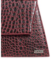 Gros plan sur un coin de sac en cuir embossé crocodile bordeaux et noir avec logo DG argenté.