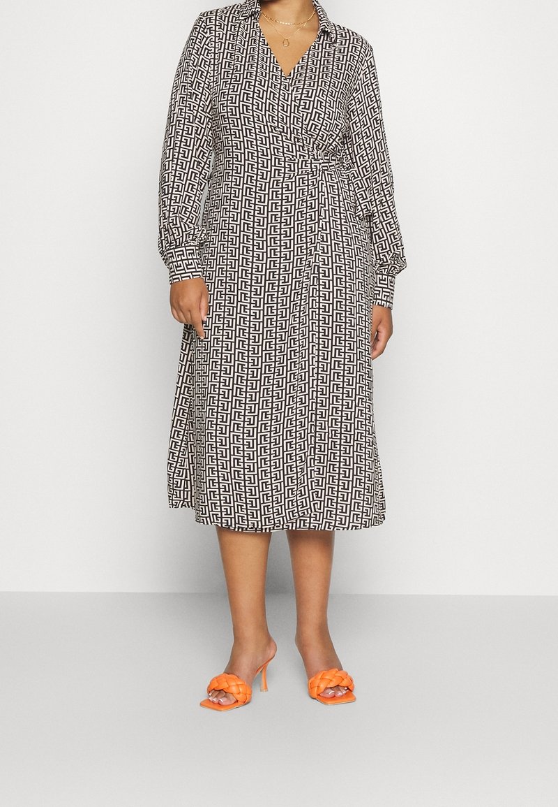 Robe portefeuille à manches longues noir et blanc avec un motif géométrique, dotée d'un col en V et d'une jupe fluide. Associée à des sandales à talons orange vif.