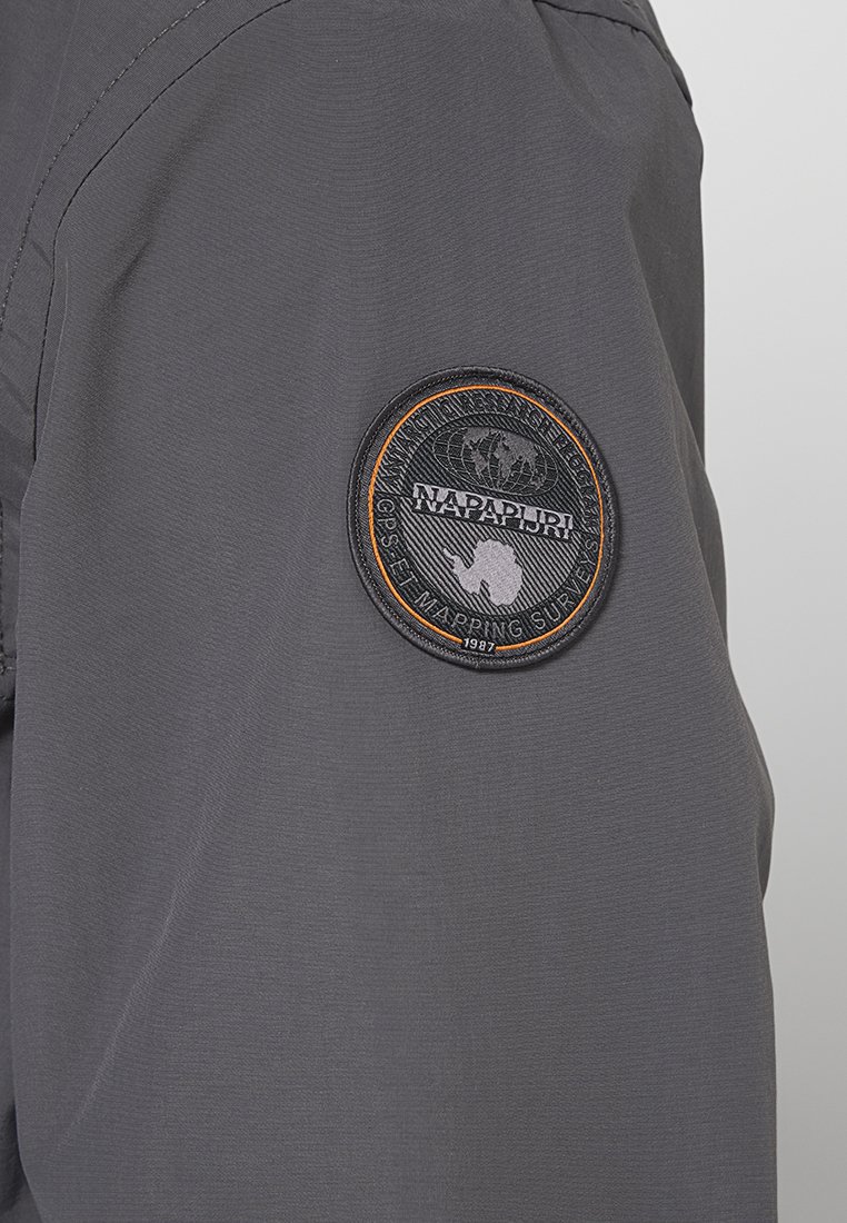 Szara kurtka z materiału z okrągłą, haftowaną naszywką z motywem globusa i napisem "Napapijri" umieszczoną na lewym rękawie.