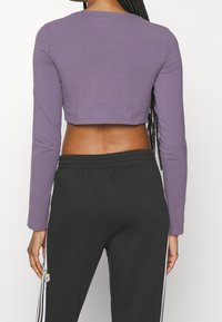 Lila långärmad crop top, figurnära design, mjuk textur; kombinerad med svarta mjukisbyxor med sidostrikar och blommig brodyr.